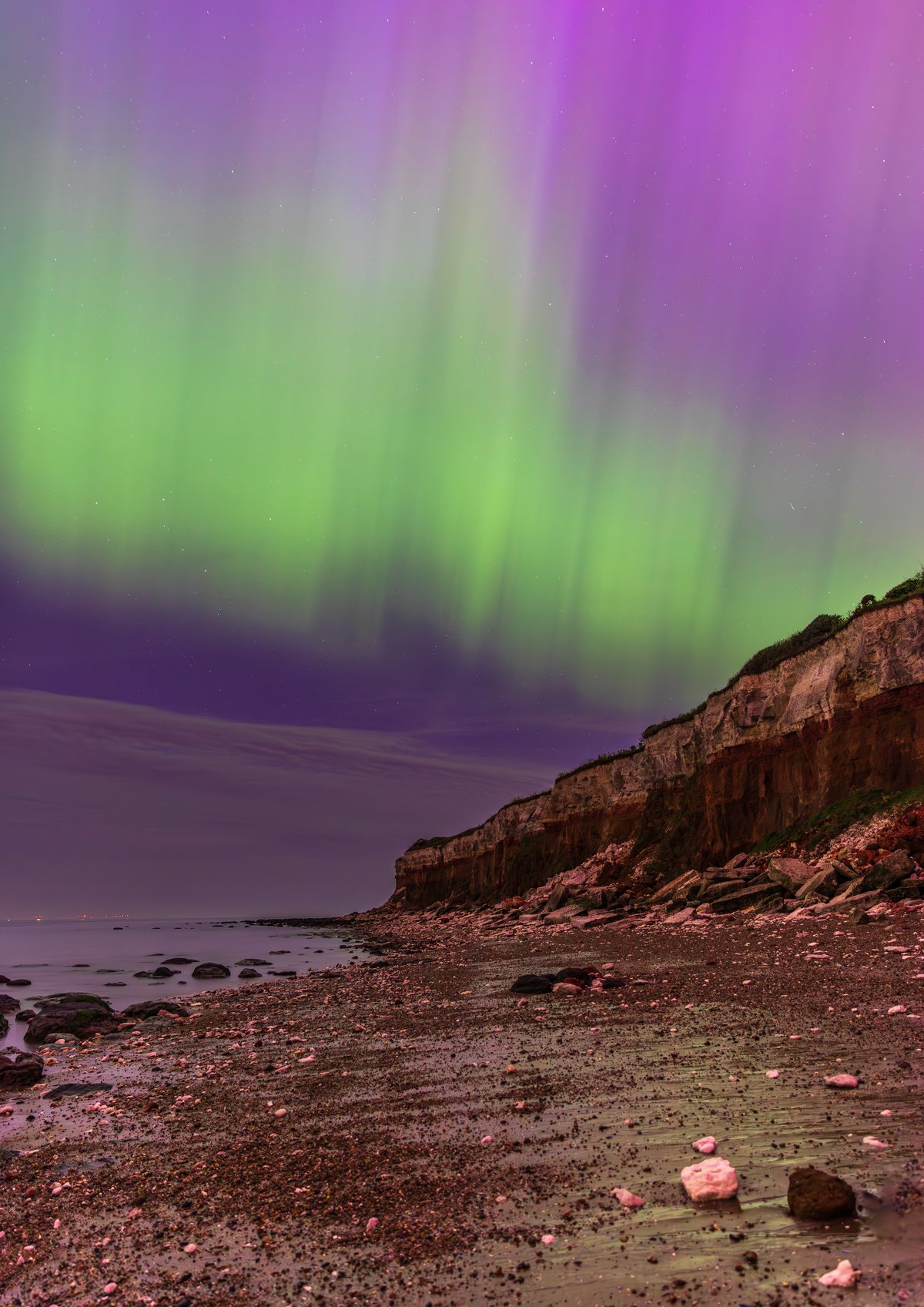 The Northern Lights in vivid green and magenta over the layered red and white cliffs at Hunstanton, Norfolk